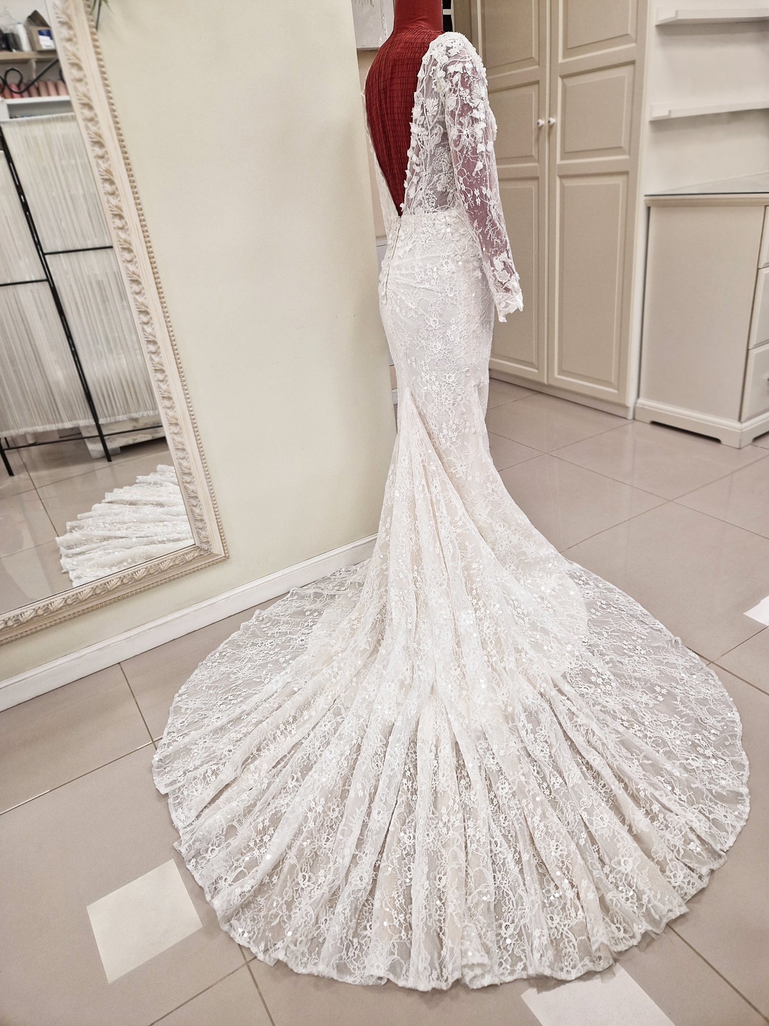 Lace wedding dress from our 2024 couture collection. The gown has a figure hugging trumpet silhouette, long sleeves, deep plunging V-neckline and V-back and lots of beading and sparkle. There is a dramatic semi-cathedral train and ruching at center back seam to beautifully shape your figure.