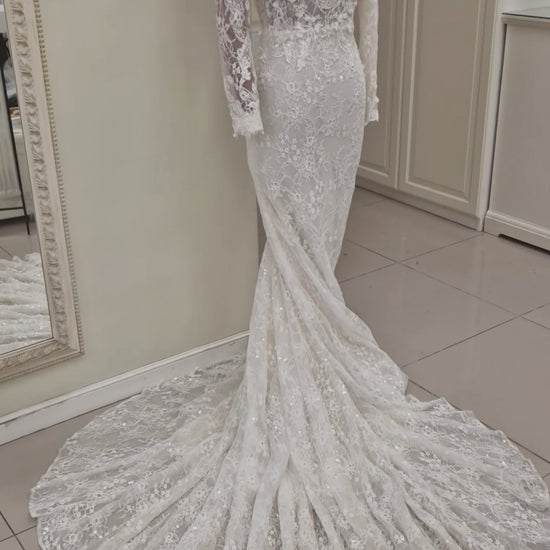 Lace wedding dress from our 2024 couture collection. The gown has a figure hugging trumpet silhouette, long sleeves, deep plunging V-neckline and V-back and lots of beading and sparkle.